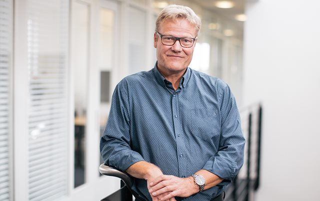 Rektor Anders Graae Rasmussen læner sig op af en trappe i gråblå skjorte