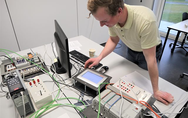 Masser af automatiserings udstyr på bord og Patrick ved panel til at styre det