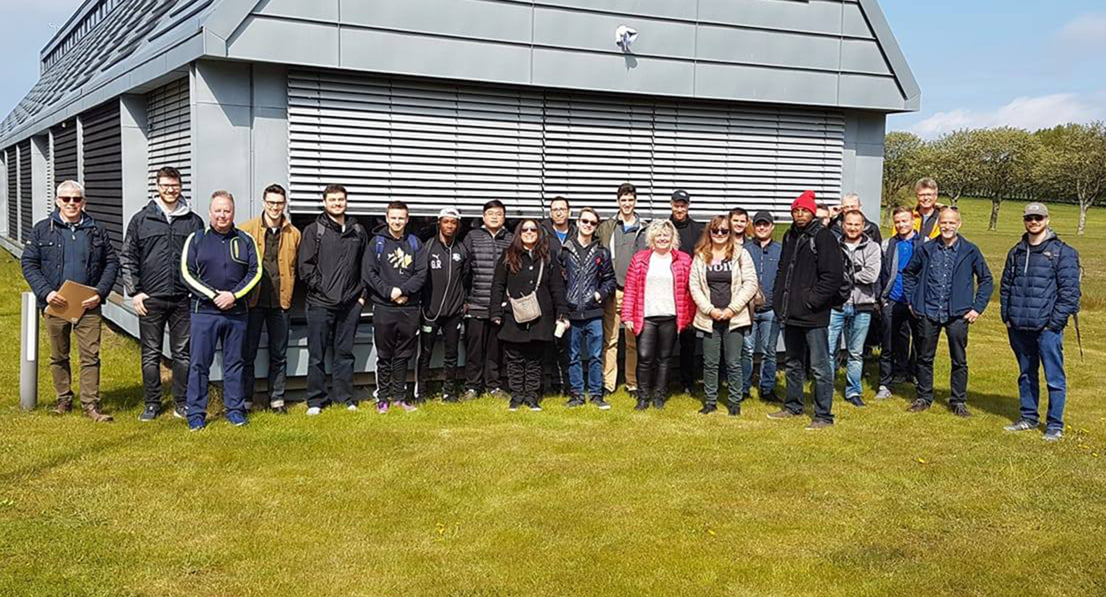 Energiteknologer stående på græsplæne foran grå bygning