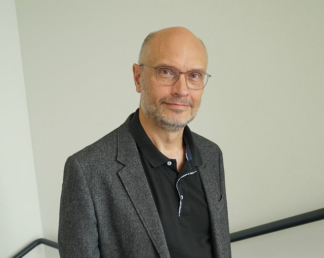 Ole Ravn smiler til dig fra trappe med hvis væg bagved