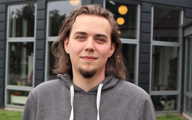 Datamatiker Levi More i sin grå hættetrøje står foran Danias campus i Grenaa