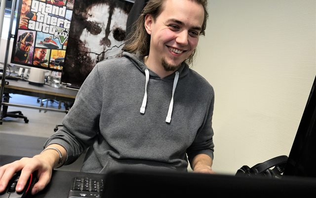 Levi Moore set fra siden, hvor han kigger på sin skærm og smiler, mens hans ene hånd hviler på sin mus