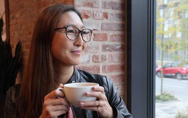 Mia kigger ud af et vindue med en kop kaffe i hænderne tæt på hovedet