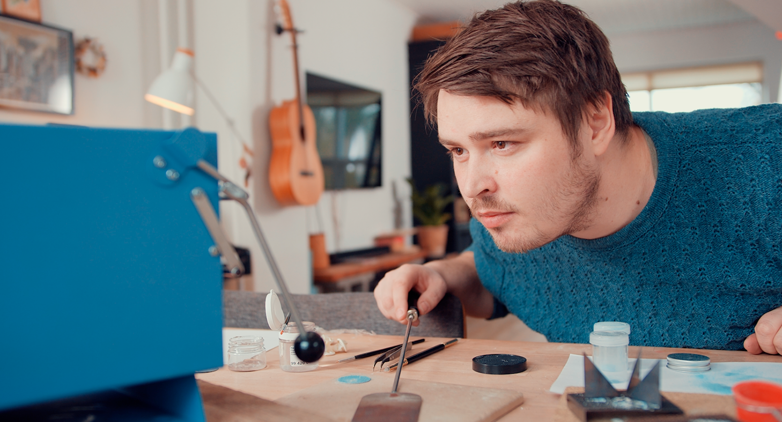 Iværksætter Kasper Reisner læner sig ind over et arbejdsbord fyldt med teknisk udstyr til at fremstille urer og kigger koncentreret på en lille lyseblå ovn.