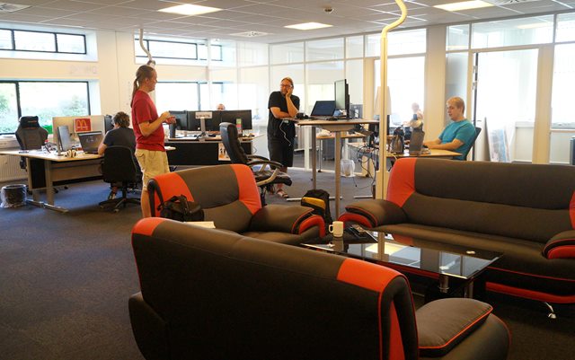 Kontorlandskab hos virksomheden Got Ethics i Holstebro. To mænd står og har en samtale over et hæve/sænke-bord, imens to andre mænd sidder og arbejder på hver sin computer i baggrunden.
