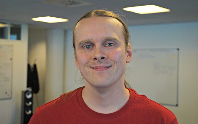 Portrætfoto af datamatiker Philip Kruse iført mørkerød t-shirt foran et whiteboard.