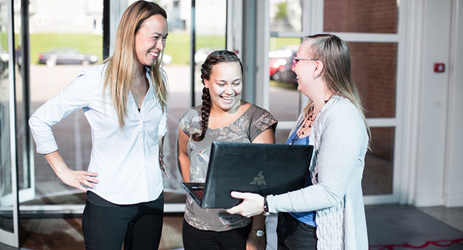 tre kvindelige studerende ser på computer og smiler