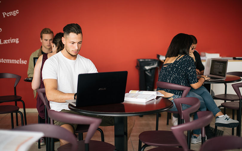Studerende sidder rundt om borde og arbejder på computer