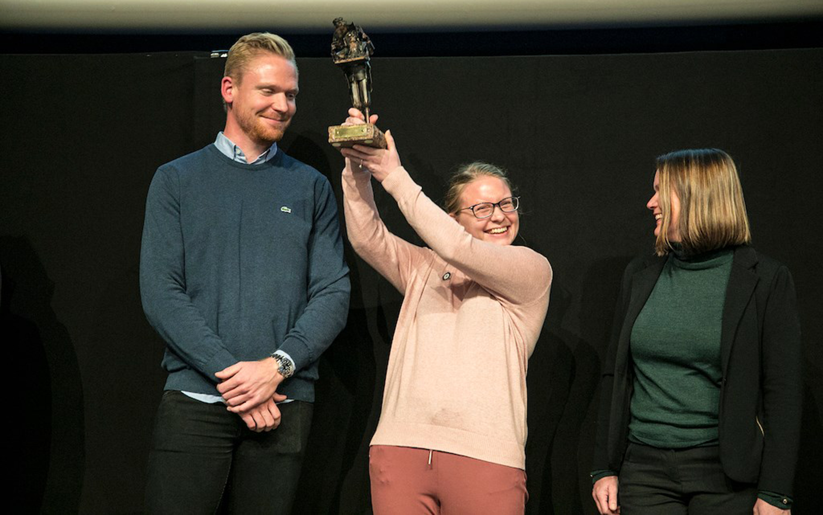 Studerende løfter vinderpokalen højt op i luften med stort smil på læben