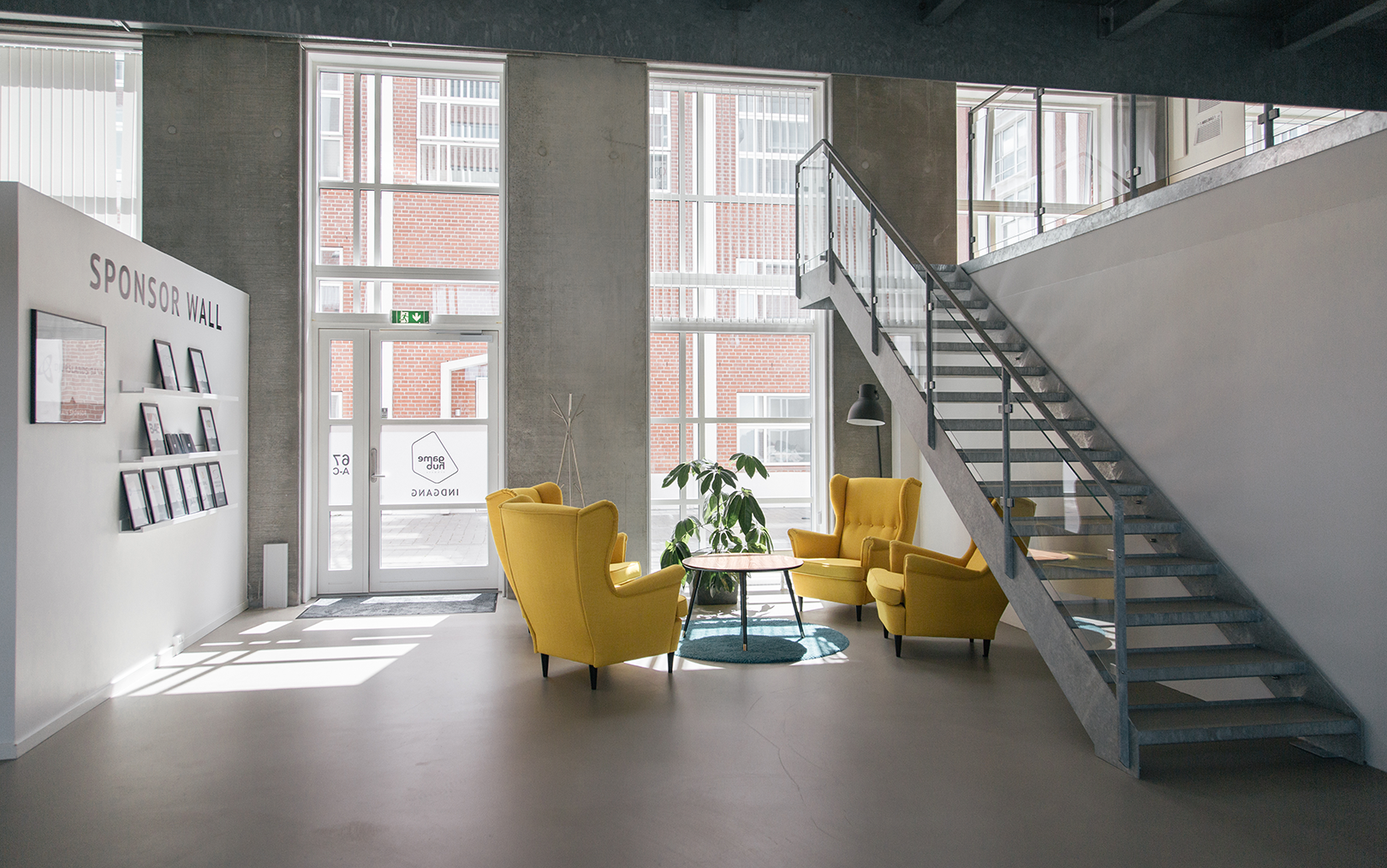 Indgangen ved Game Hub Denmark med gule lænestole om bord, grå betonvægge og trappe op på 1 sal.