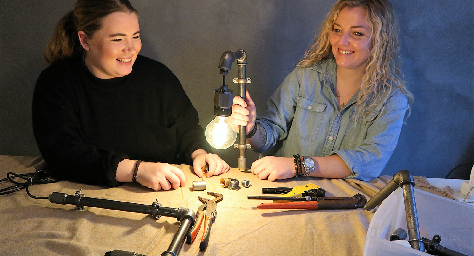 Serviceøkonomerne Cecilie og Lisbeth med en lampe lavet af vandrør og lys i imellem sig