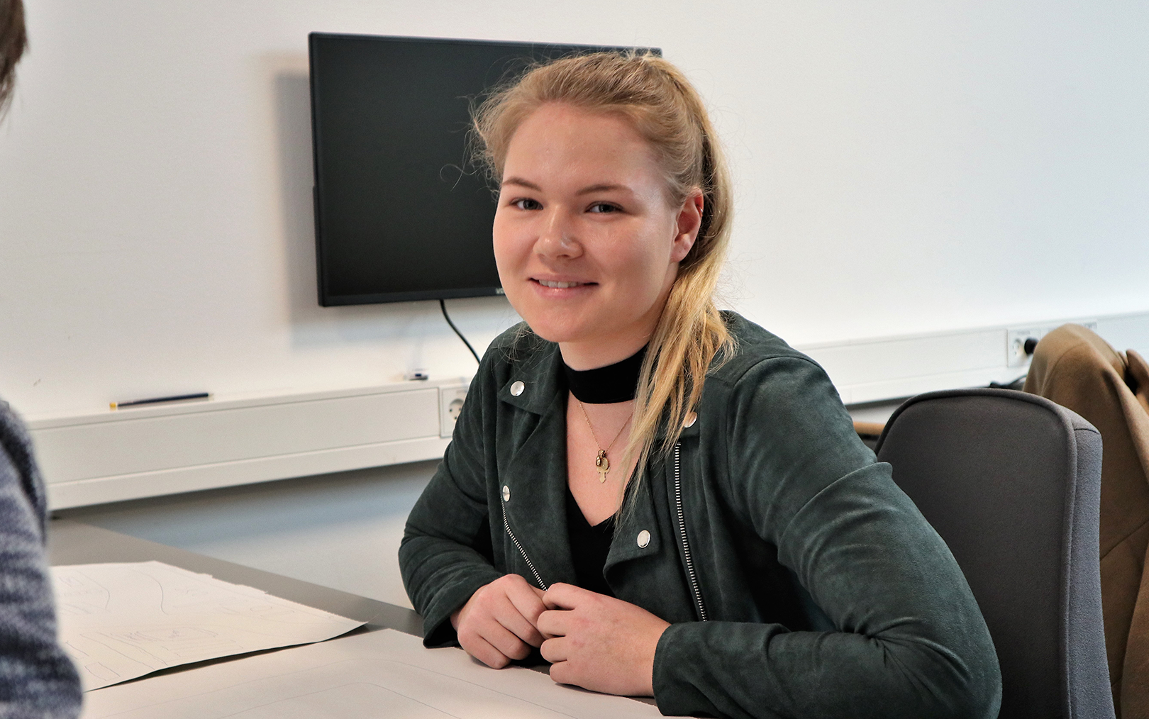 Smilende Louise midt i gruppearbejde på markedsføringsøkonom studiet med sort skærm i baggrunden