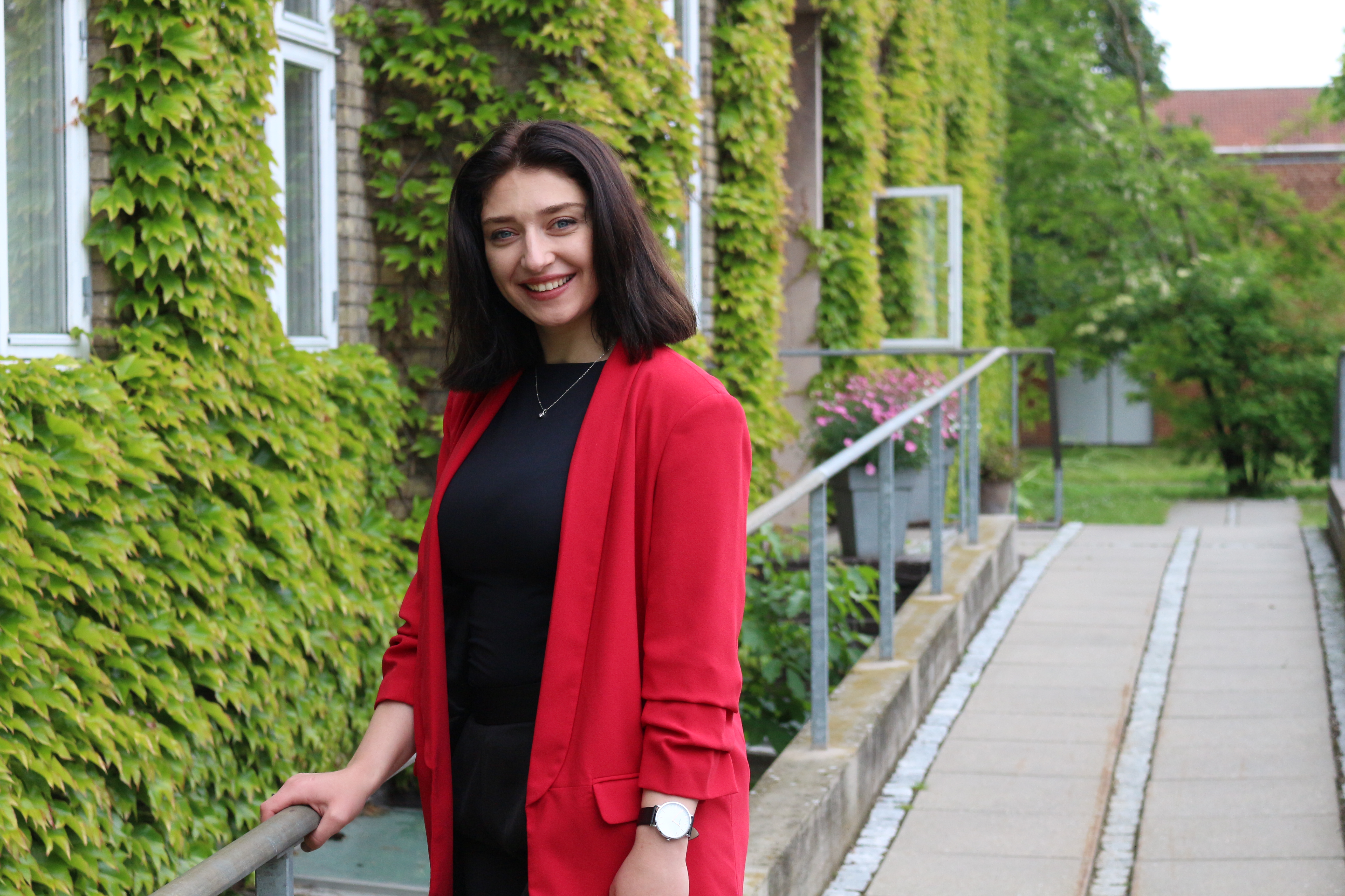 Elena holder ved gelænder udenfor bygning dækket af grønne blade