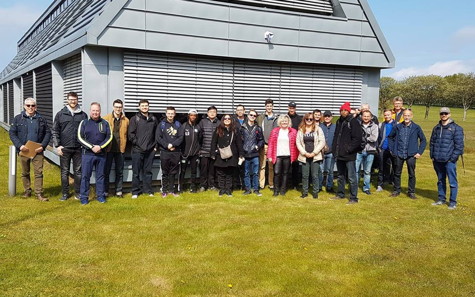 Energiteknologer stående på græsplæne foran grå bygning 