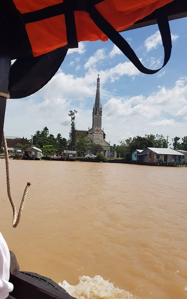 Kirke set fra båd med brunt vand i forgrunden