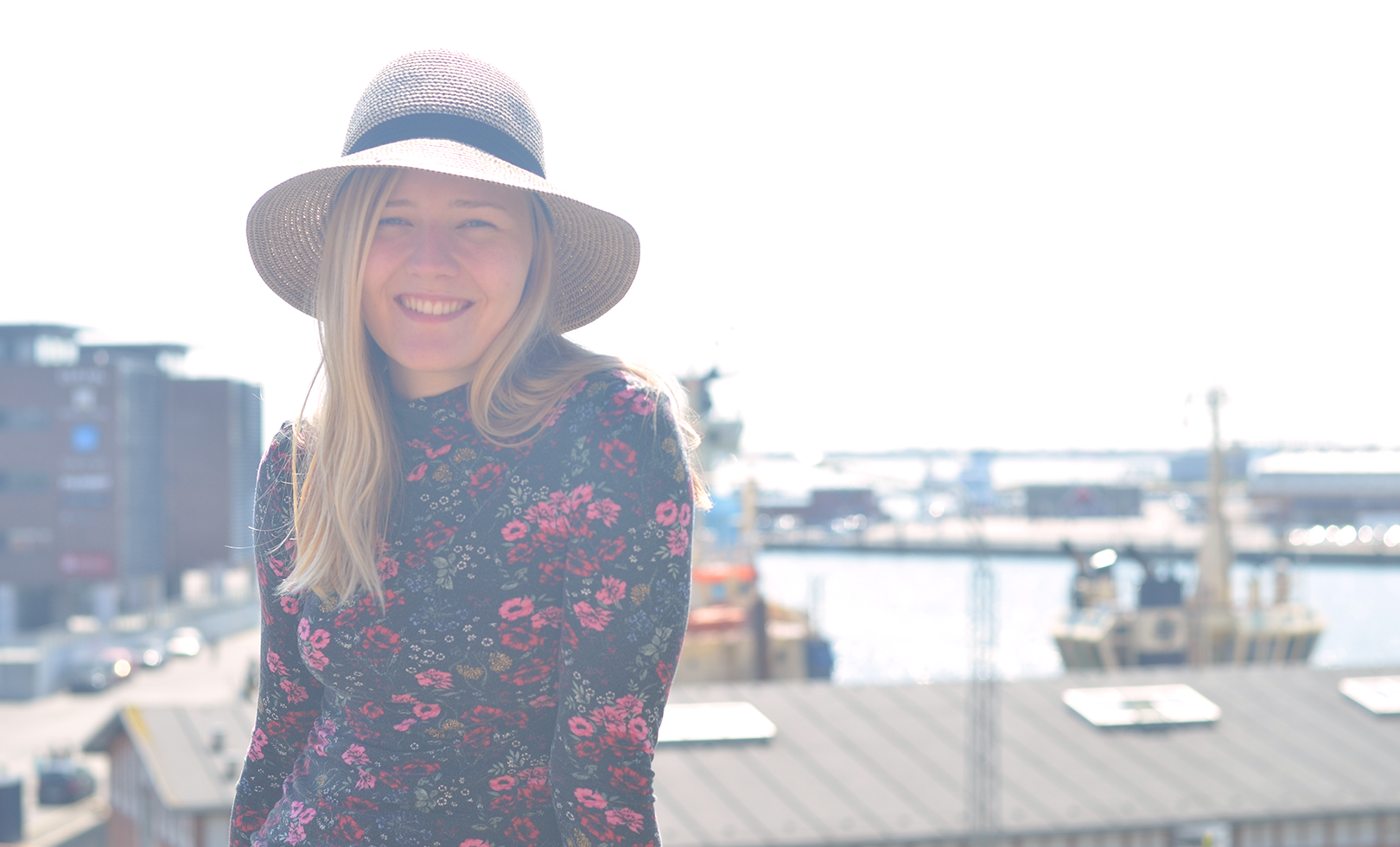 Stinna i blomstret trøje med hat på foran havn