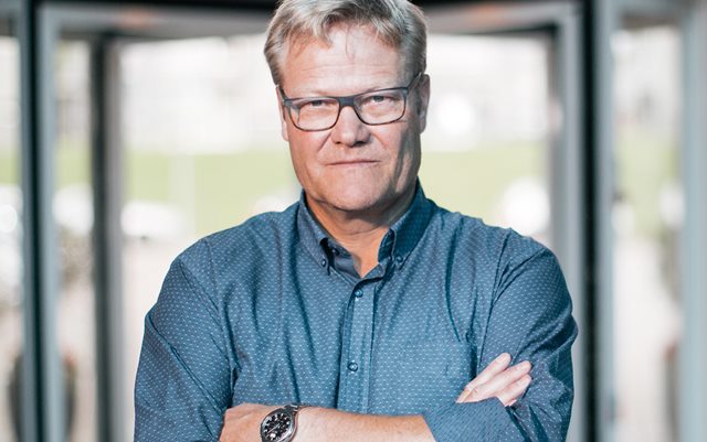 Anders Graae Rasmussen med korslagte arme og fast blik i gråblå skjorte