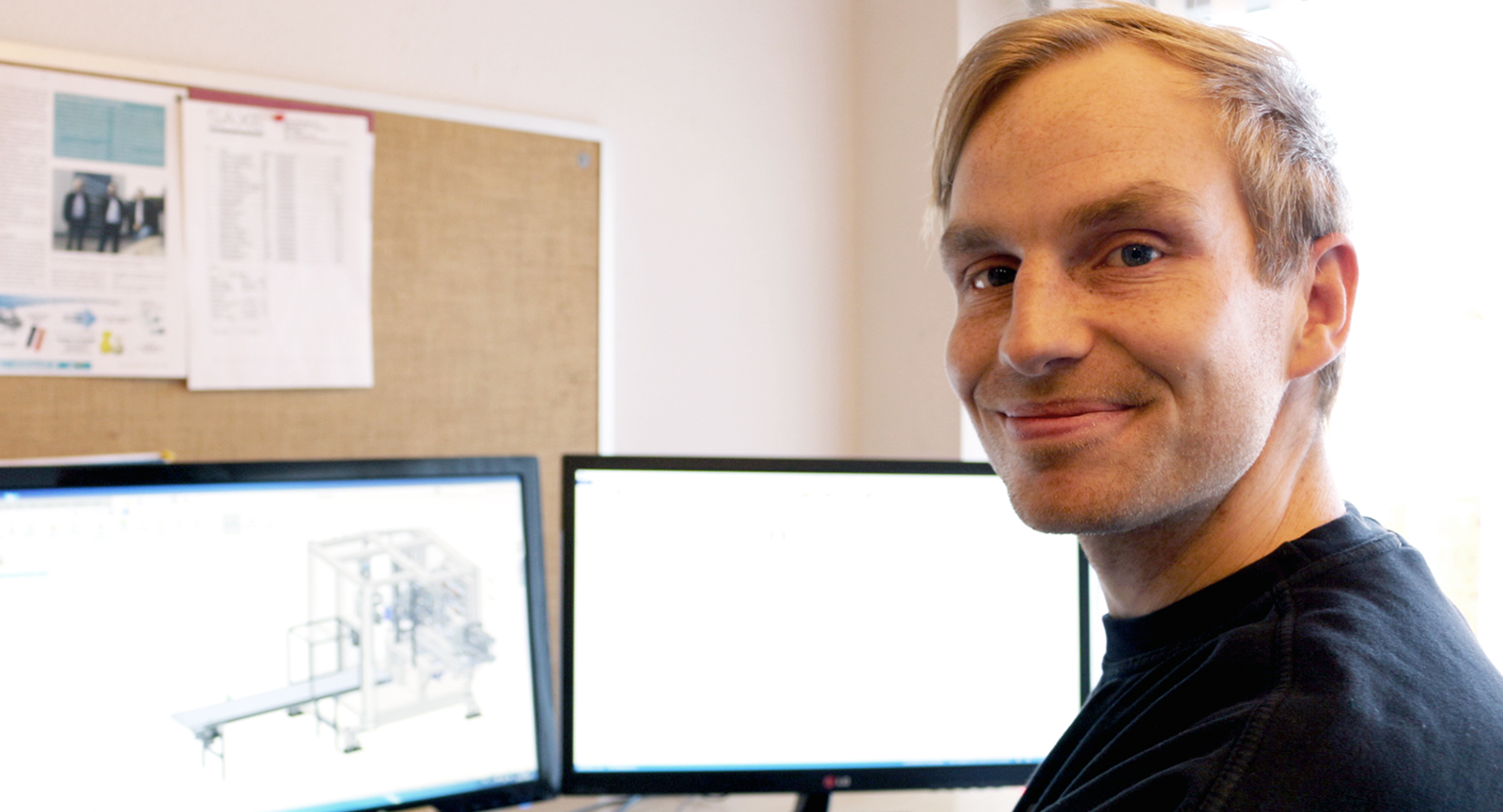 Morten smiler ved sit skrivebord med to skærme i baggrunden