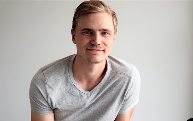 Automationsteknolog Max smiler til dig op af hvis væg i grå t-shirt