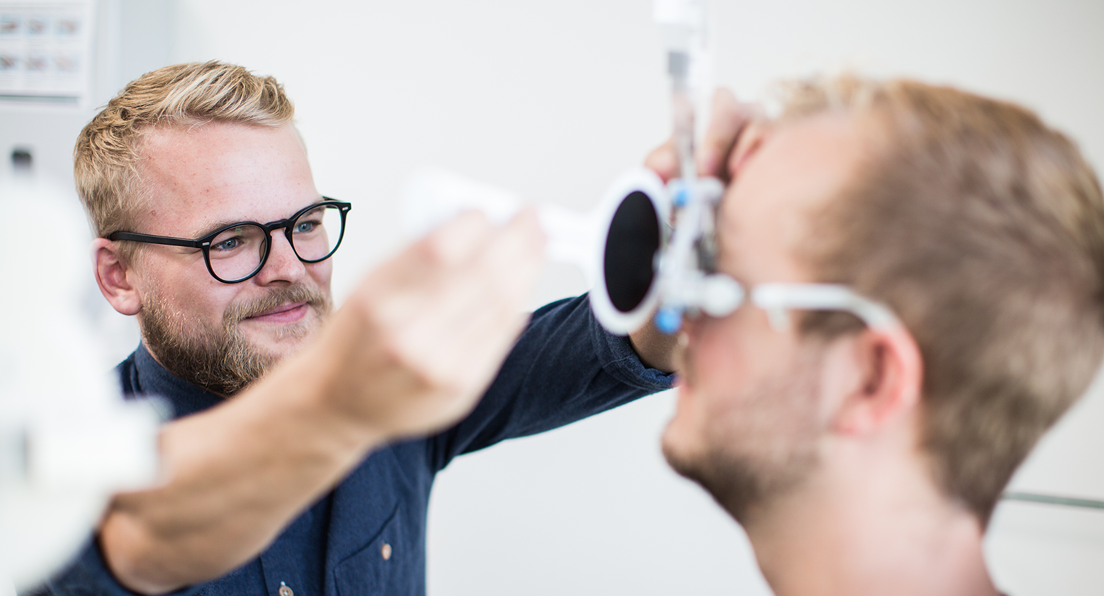 Optiker studerende øver sig på patient med en skør brille på at lave synsundersøgelse