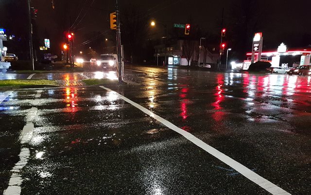 Rengvådt lyskryds i Vancouver om natten med genskær af røde lys i den våde asfalt 