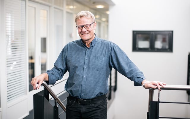 Anders Graae Rasmussen griner, mens han med begge hænder holder ved en trappe i gråblå skjorte