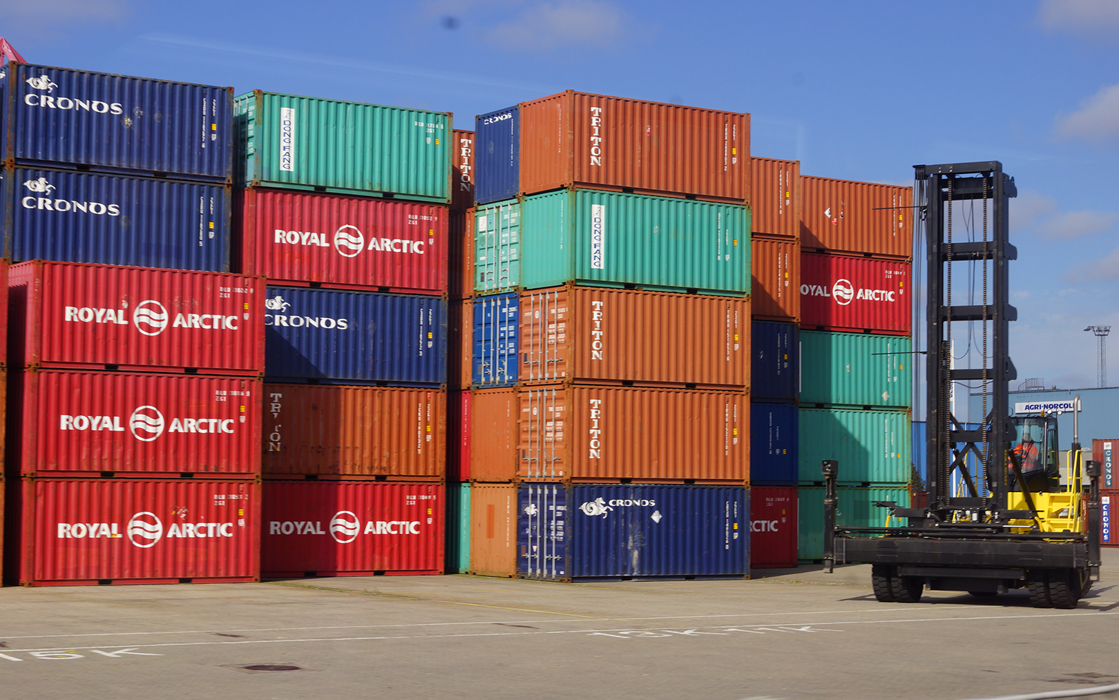 Mange containere ovenpå hinanden på havn med containerlastbil i siden