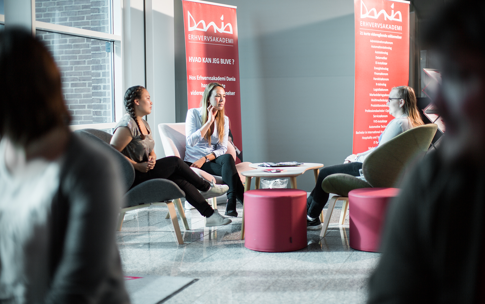 Tre kvindelige studerende sidder i tre lænestole og snakker sammen ved indgangen på Erhvervsakademi Dania i Randers