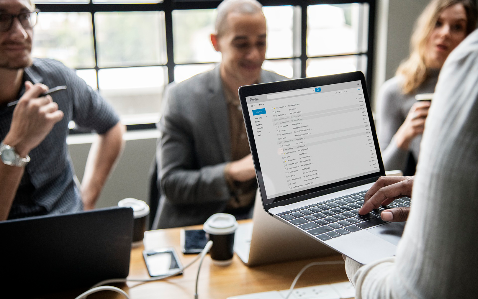Person holder en computer, der er tydelig, mens vedkommende snakker med tre kolleger om en opgave