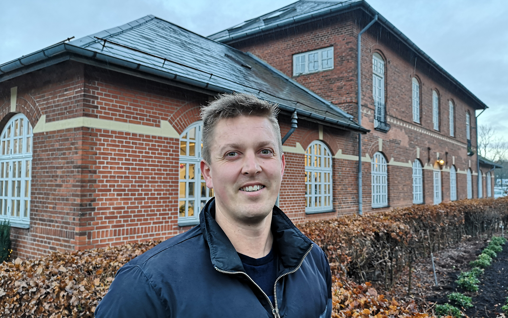 Finansøkonom-studerende Kristian Kock Pedersen smilende foran den gamle stationsbygning i Hammel.