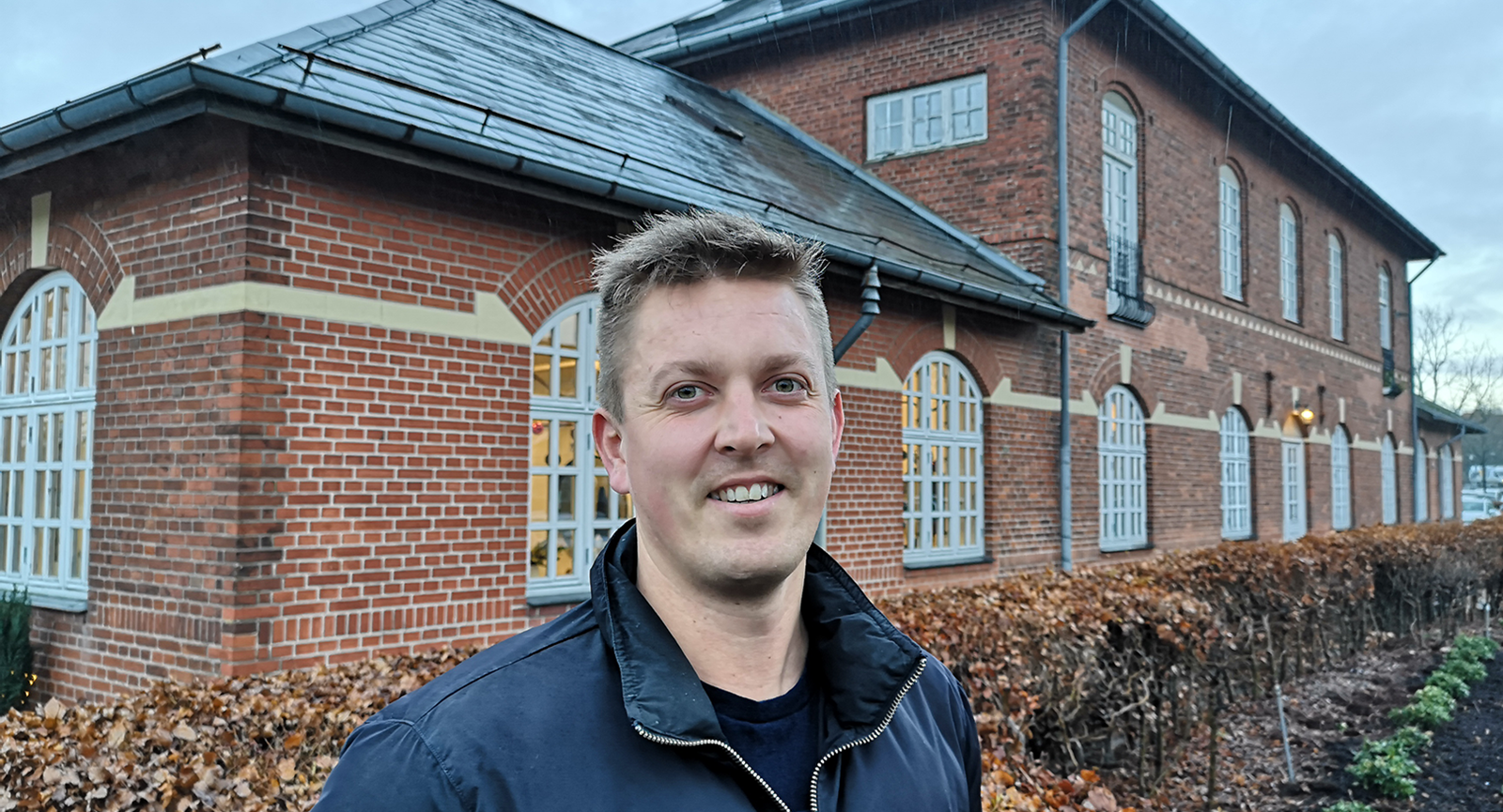 Finansøkonom-studerende Kristian Kock Pedersen smilende foran den gamle stationsbygning i Hammel.