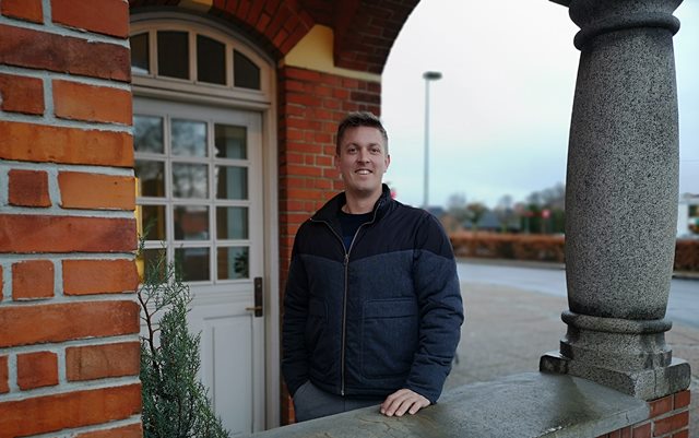 Finansøkonom-studerende Kristian Kock Pedersen smilende foran døren til den gamle stationsbygning i Hammel.