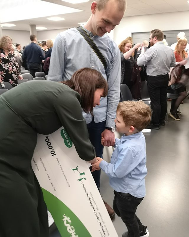 Optometrist Anette Kjær Nordborg holder et stort paplegat på 10.000 kroner, mens hun bukker sig ned for at tale med sin søn