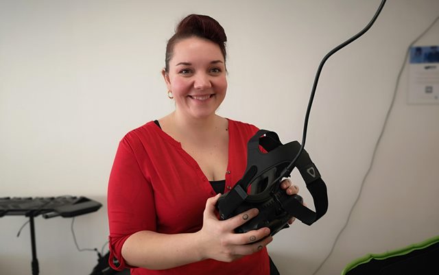 Erin Gertsen smiler til kameraet, imens hun holder et par sorte virtuel reality-briller i hænderne.