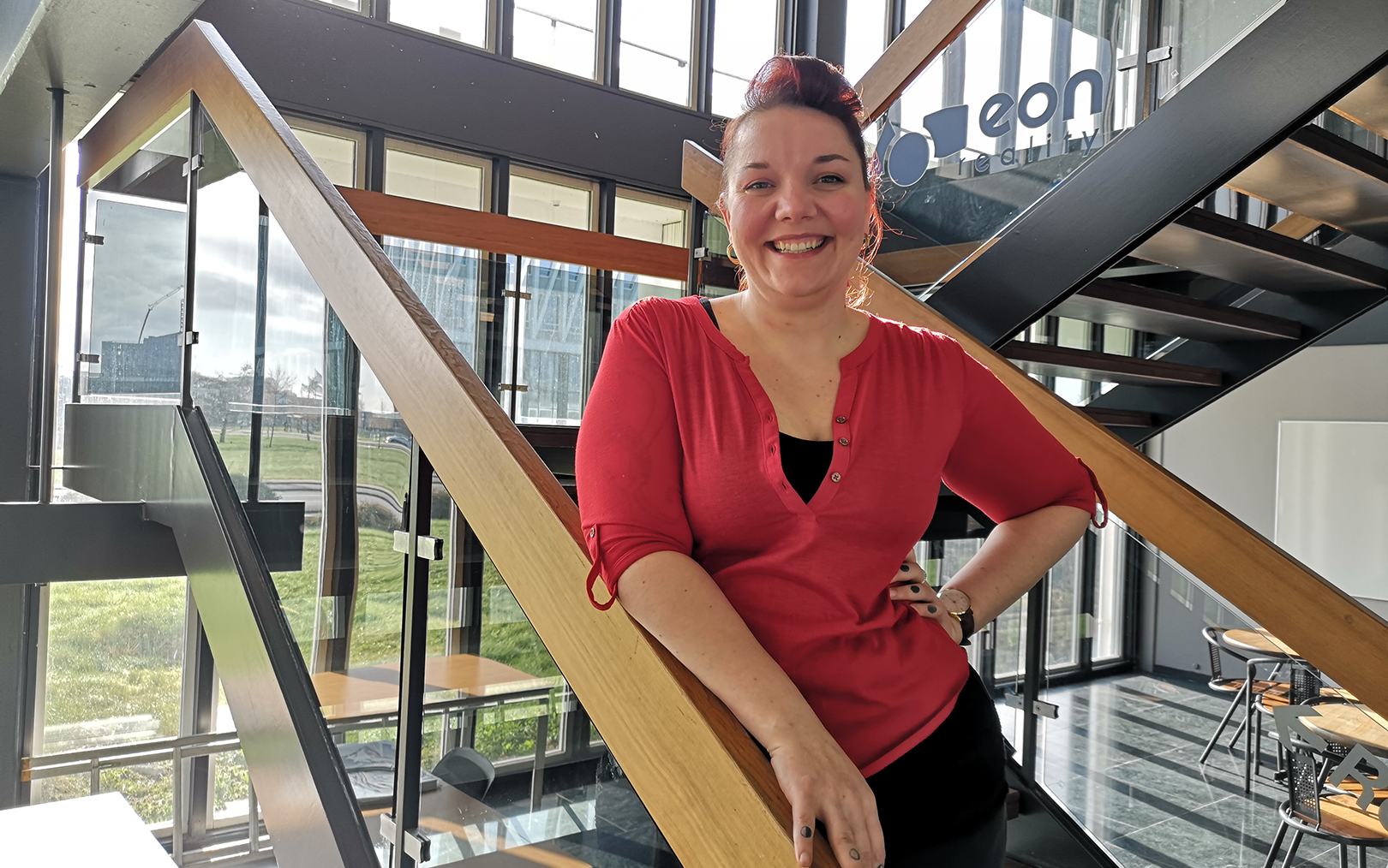 Erin Gertsen står på en trappe og læner sig op ad gelænderet, imens hun smiler stort til kameraet.