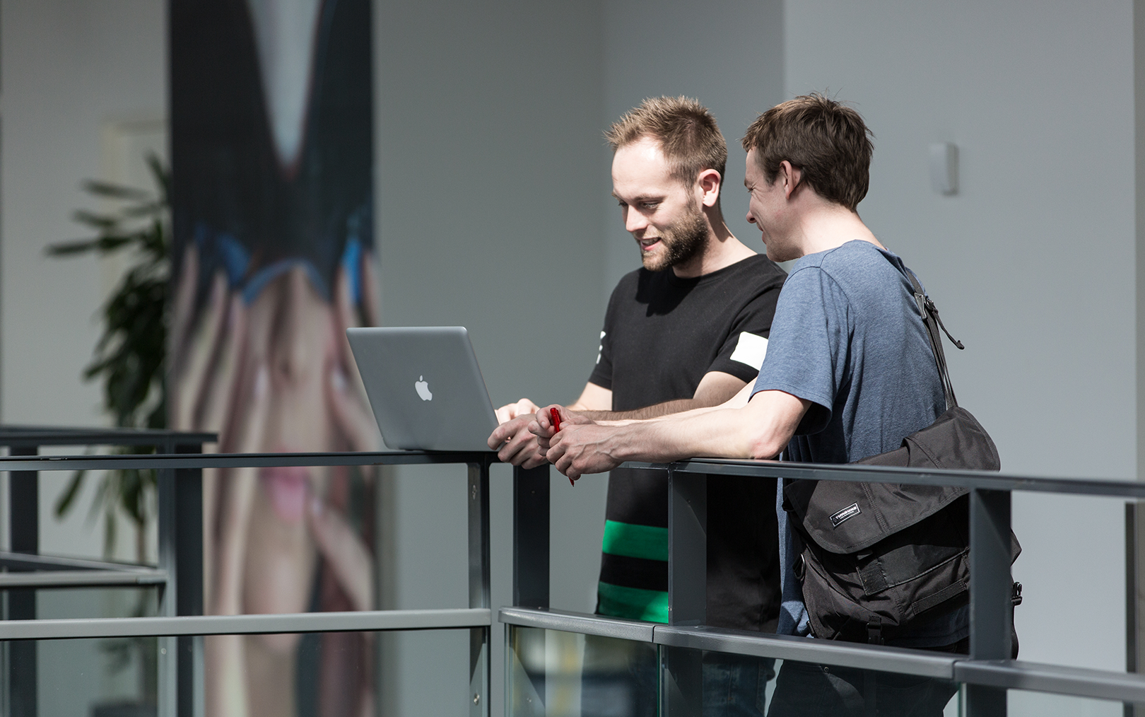 To mandlige studerende læner sig op ad et gelænder, imens de begge kigger på en bærbar computer.