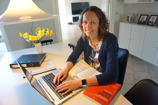 Sagsbehandler Luise Korsgaard sidder ved sit spisebord og arbejder på en bærbar computer, imens hun smiler til kameraet.