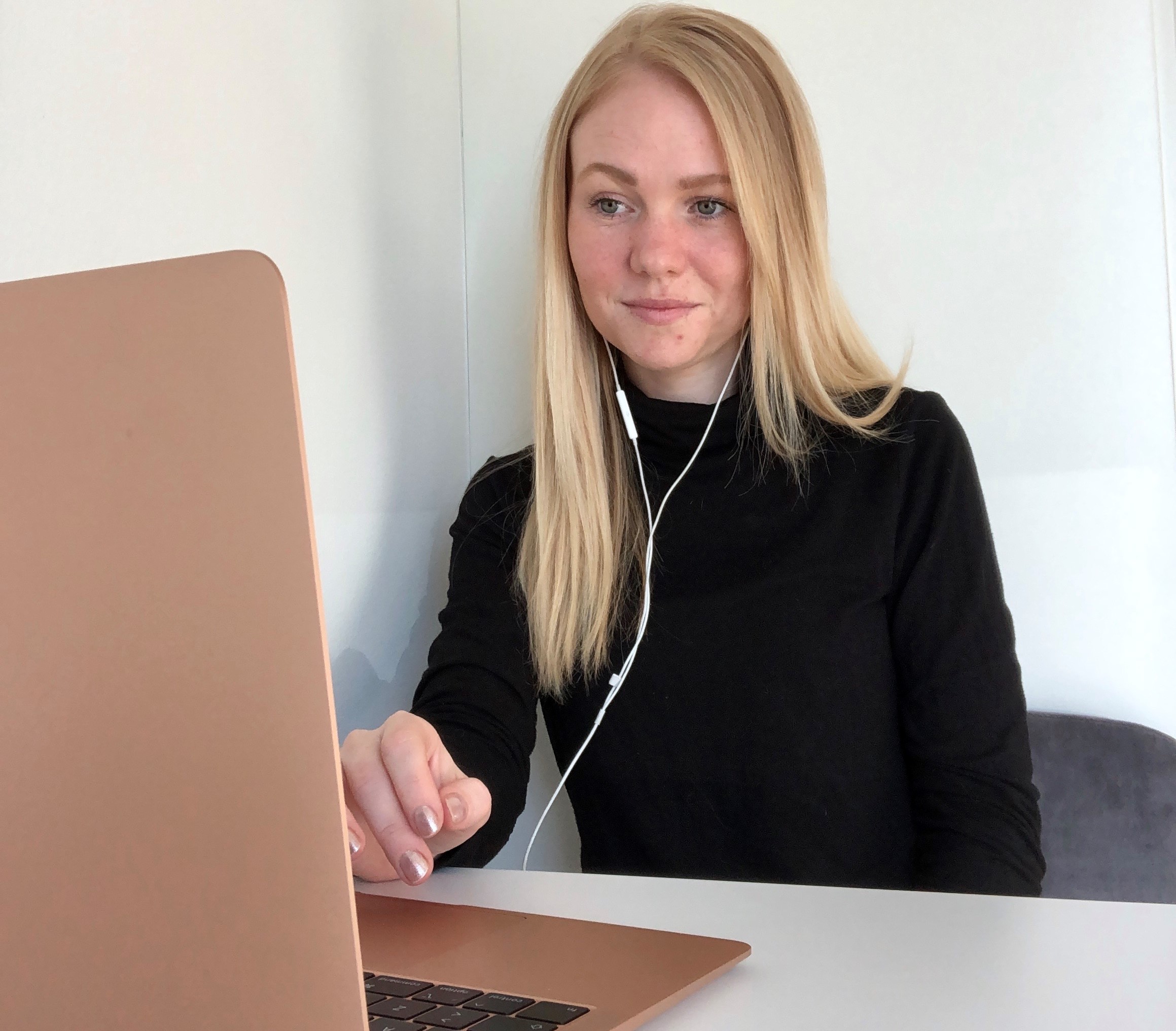 Markedsføringsøkonomstuderende Sara la Cour sidder ved et skrivebord og kigger på en bærbar computer med høretelefoner i ørerne og fingrene svævende over tastaturet.