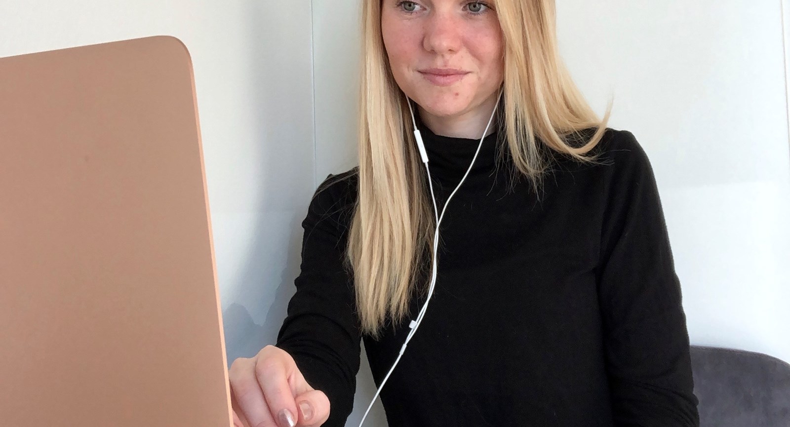 Markedsføringsøkonomstuderende Sara la Cour sidder ved et skrivebord og kigger på en bærbar computer med høretelefoner i ørerne og fingrene svævende over tastaturet.