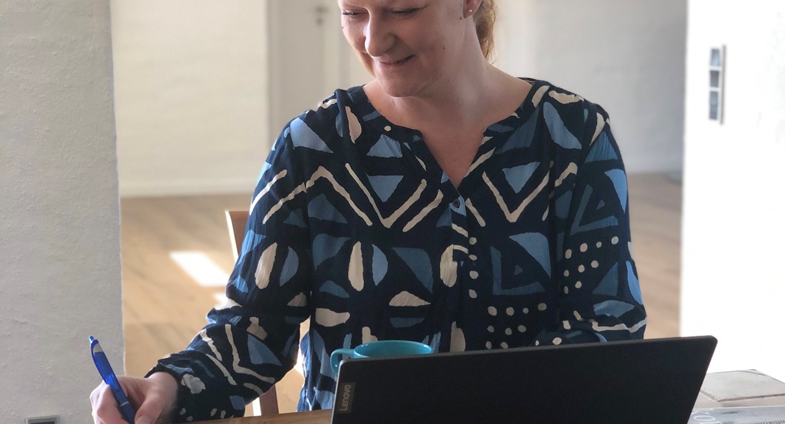 Socialrådgiver Diana Laursen tager noter på en notesblok, mens hun sidder ved et spisebord foran en bærbar computer og holder om en lyseblå kaffekop.