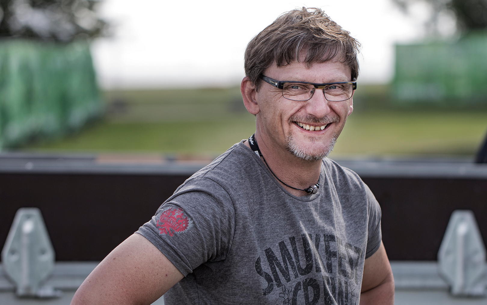 Handelsøkonom Søren Mylund Pedersen smiler til kameraet iført en grå t-shirt med påskriften 'Smukfest Crew'.