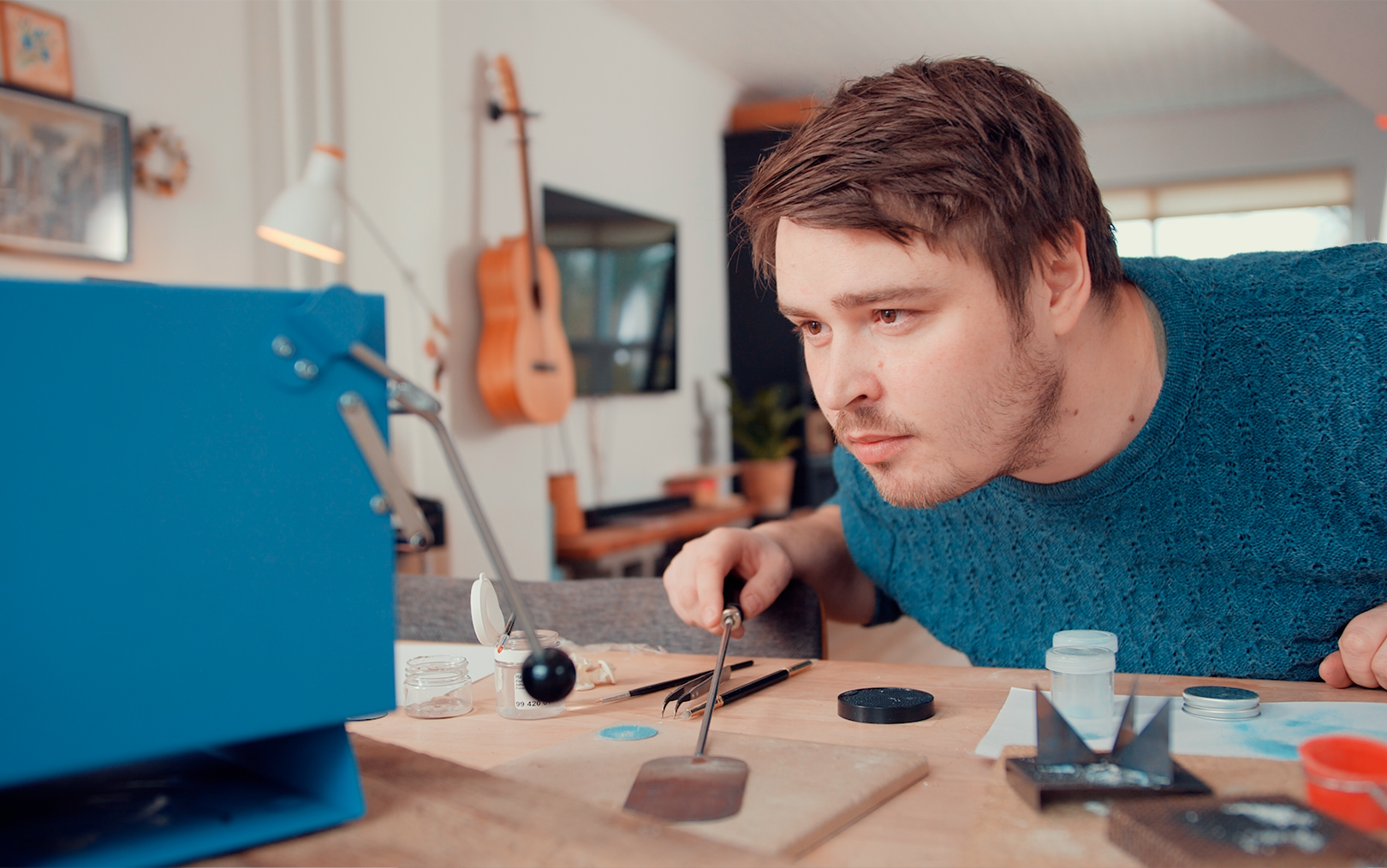 Iværksætter Kasper Reisner læner sig ind over et arbejdsbord fyldt med teknisk udstyr til at fremstille urer og kigger koncentreret på en lille lyseblå ovn.