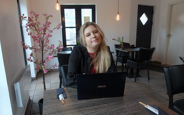 Lasma Balode, som er studerende fra Letland, sidder på en café ved et lille bord med en bærbar computer og kigger mod kameraet. 