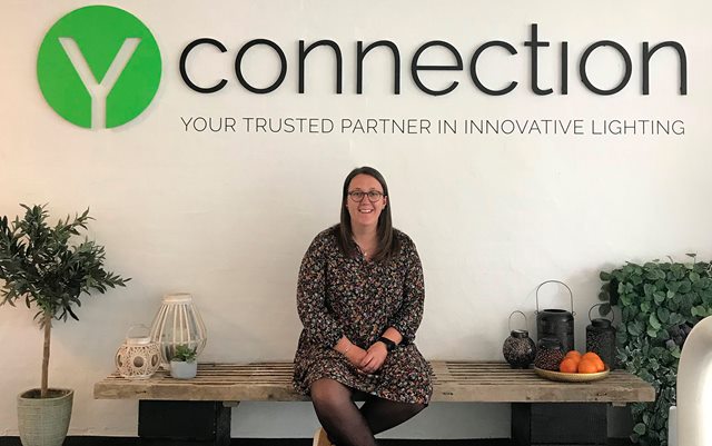 Handelsøkonom-studerende Anette Svith Mortensen sidder på en bænk under et stort virksomhedslogo med påskriften Y Connection, hvor hun er i praktik.