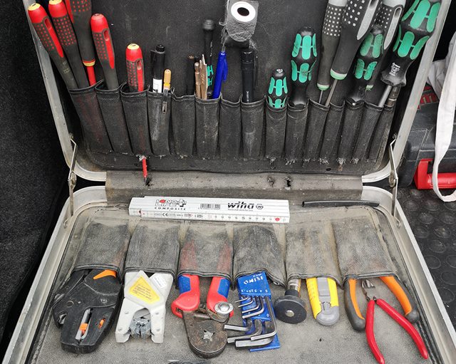 En åben kuffert med værktøj. I låget ses en række røde og grønne skruetrækkere og et par blyanter. I bunden en række forskellige tænger og et umbraco-nøglesæt.