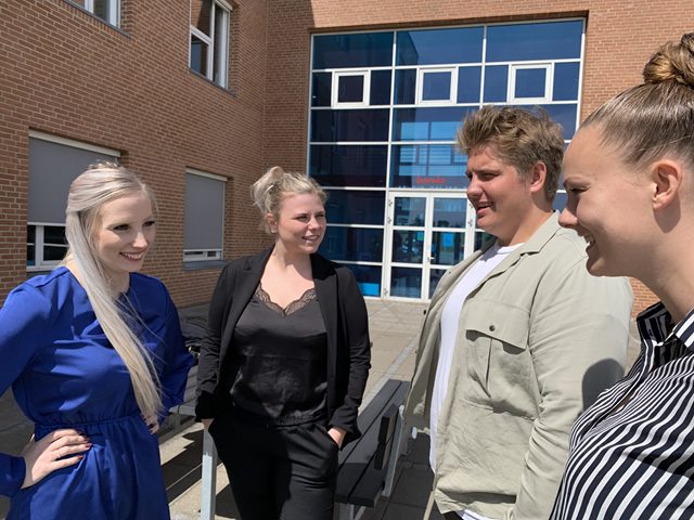 Fire markedsføringsøkonom-studerende står uden for Erhvervsakademi Dania i Randers og taler sammen i solskinnet. 