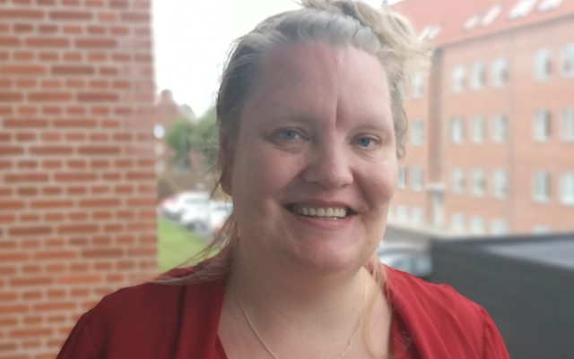 Portrætbillede af social- og sundhedshjælper Tanja Rasmussen, der at søgt ind på uddannelsen til administrationsøkonom. Tanja står på en altan i en rød murstensbygning og smiler til kameraet.