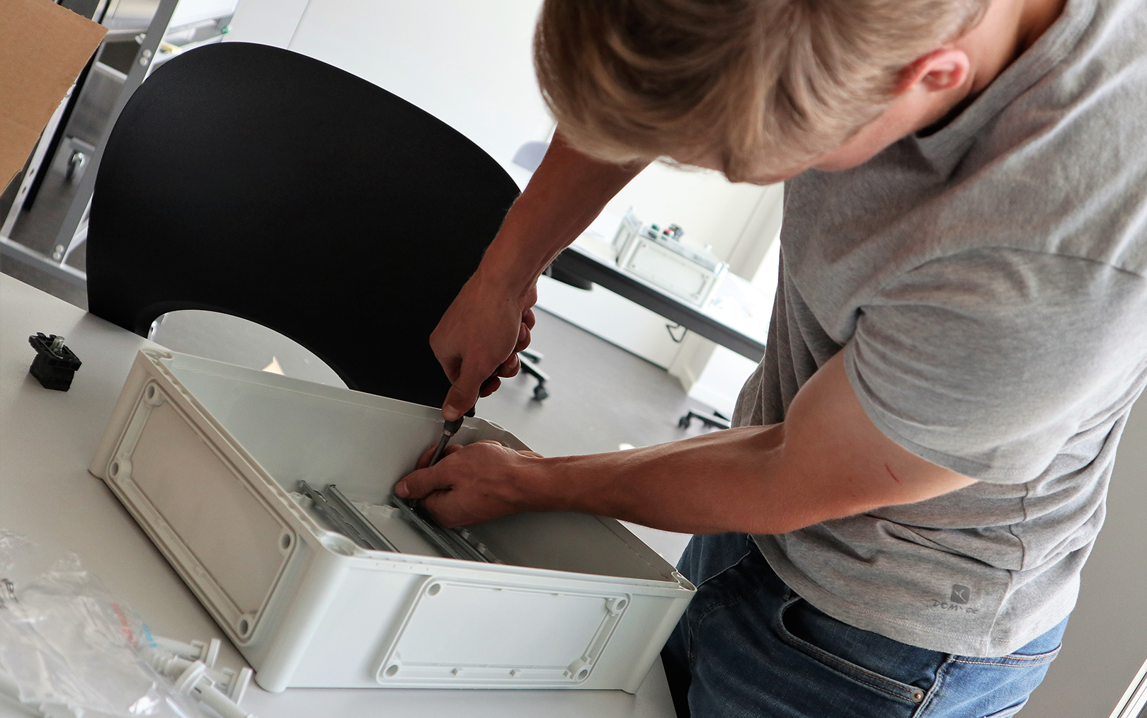 Portrætfoto af automationsteknologstuderende Max Høgh-Pedersen skruer noget fast på indersiden af en plastikkasse. Han står bøjet over kassen, mens han arbejder.