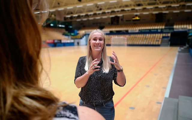 Rikke Sørensen står i håndboldhal og samtaler med kvinde