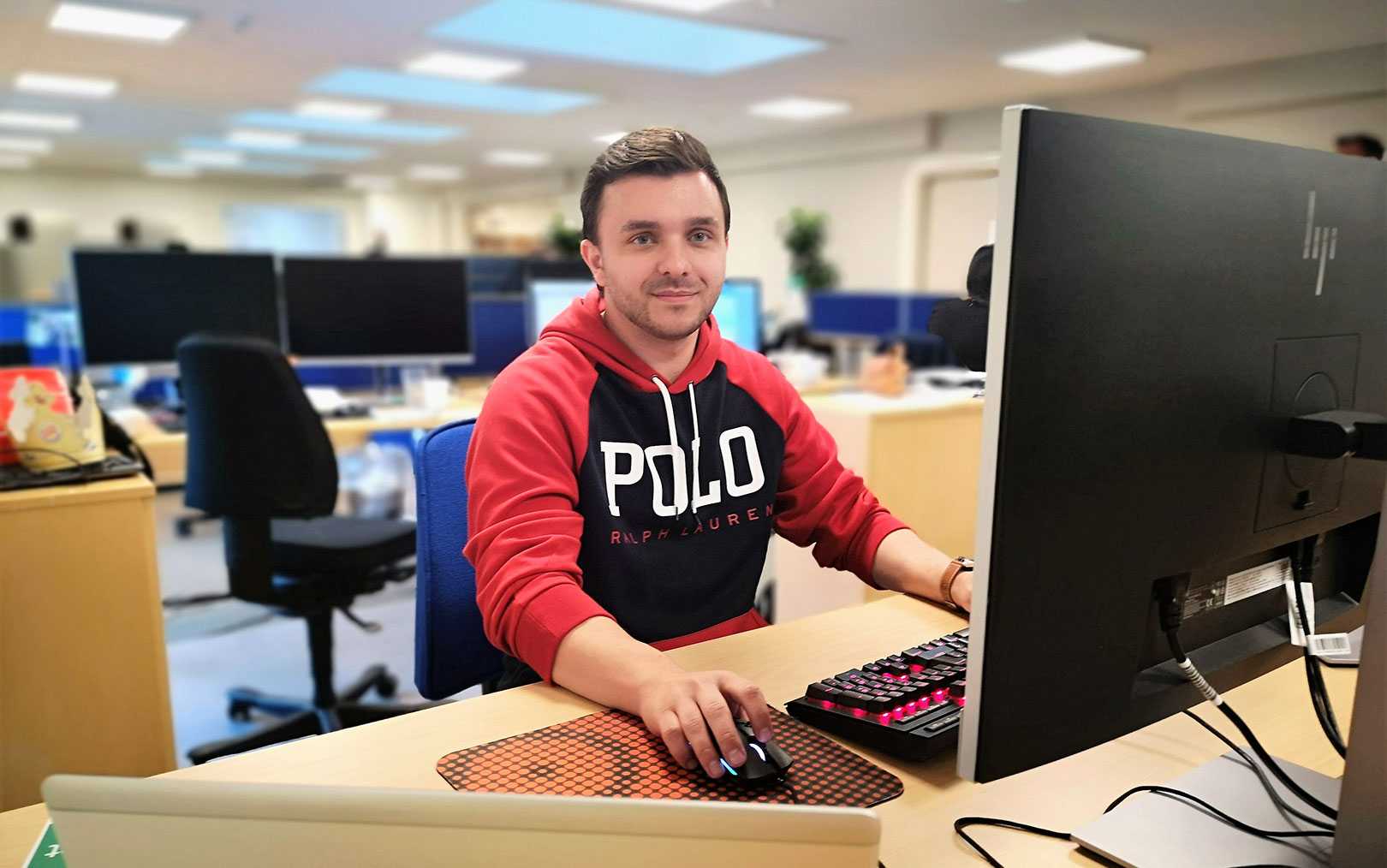 Mirza sidder ved sin computer i storerumskontor med en hånd på sin mus og en på tastatur